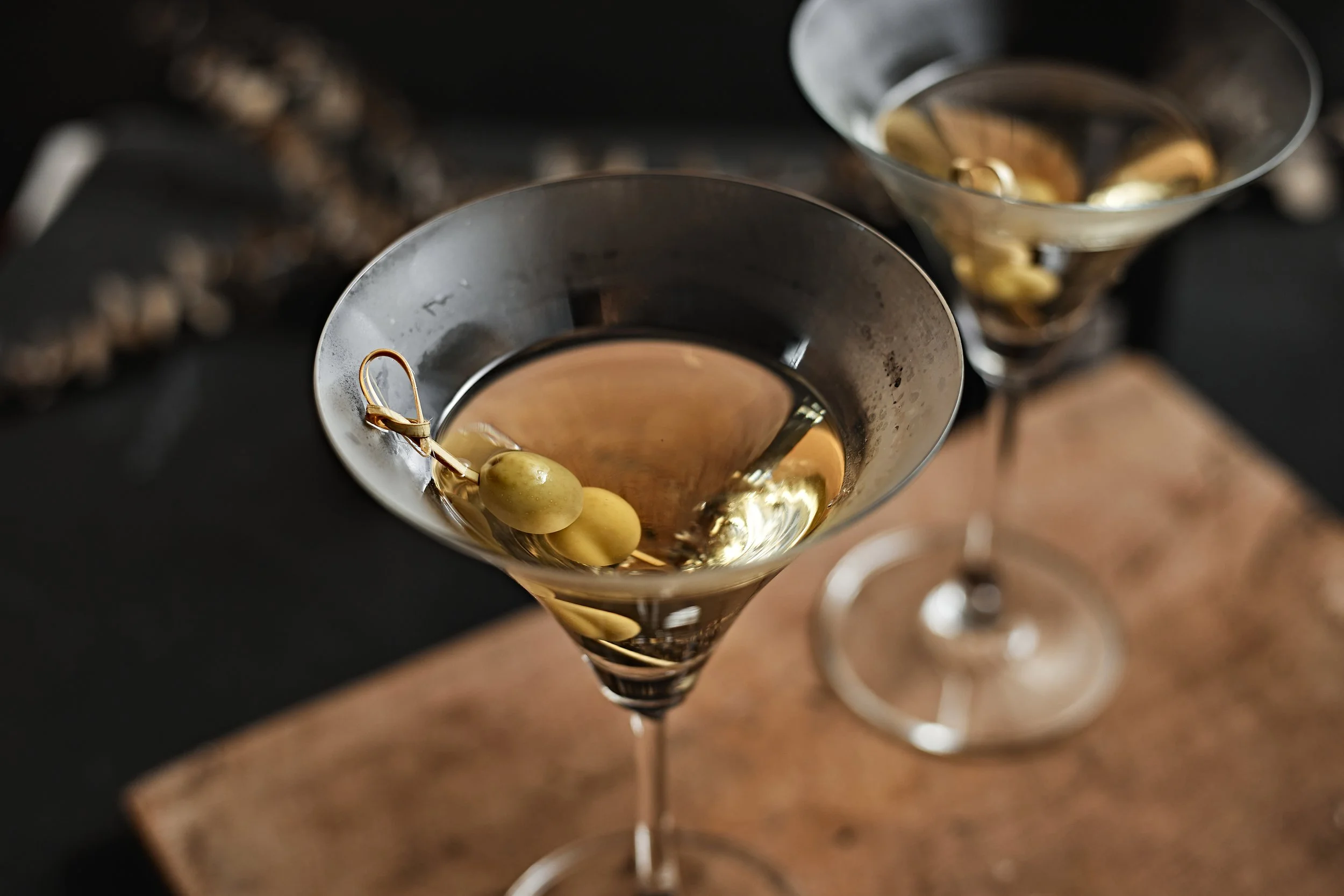 Two martini glasses filled with a golden cocktail garnished with green olives.