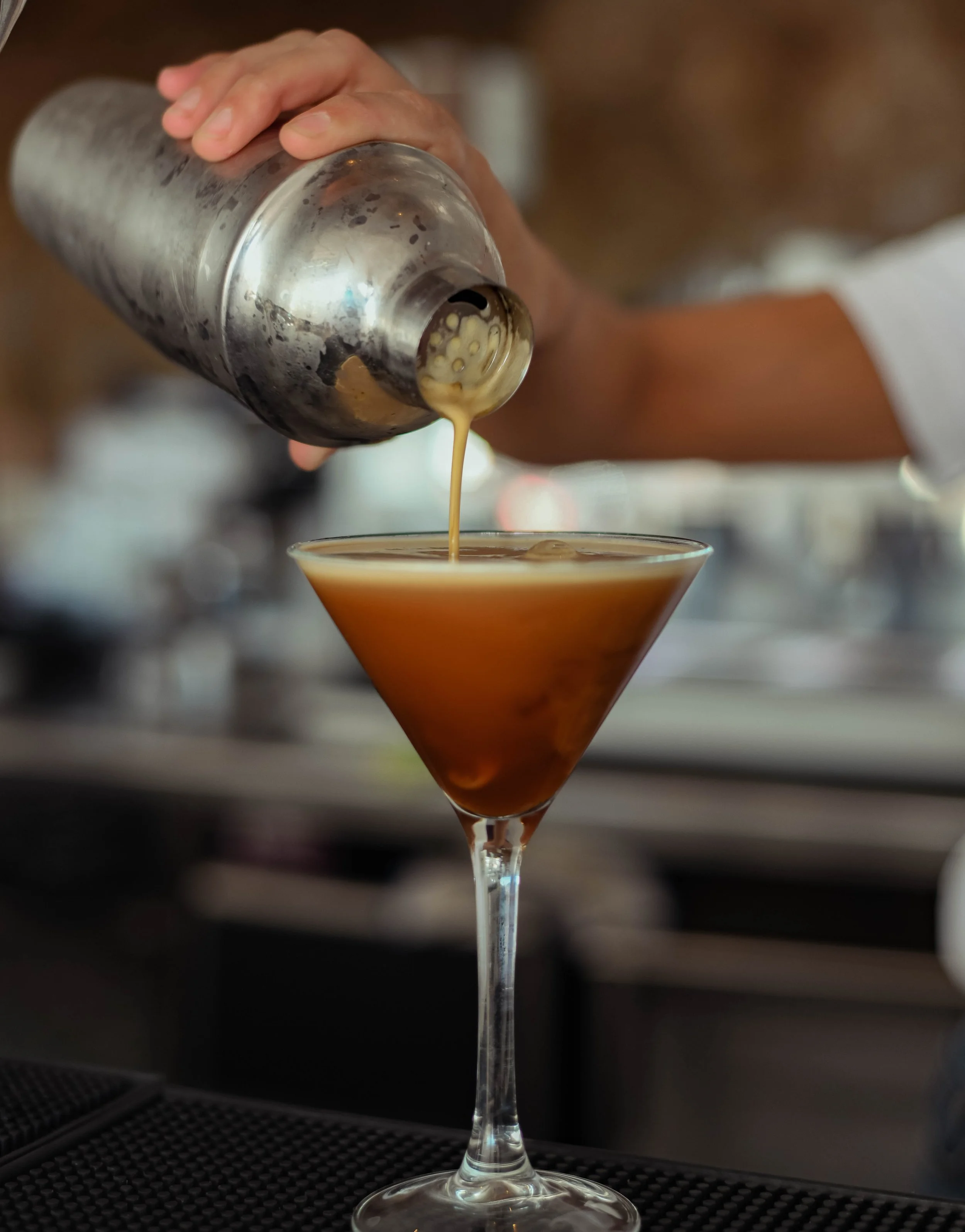 Bartender pouring coffee liqueur into a cocktail glass for a dessert drink.