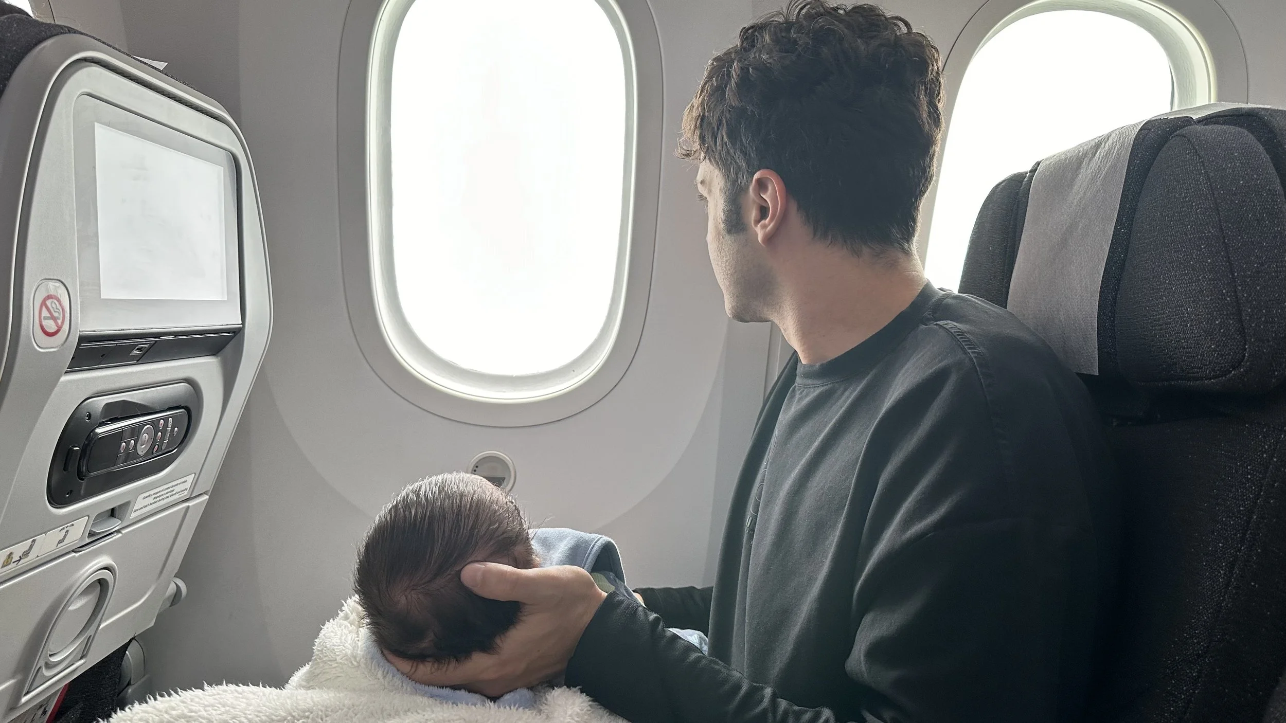 A man holding a newborn baby on an airplane, looking out the window.