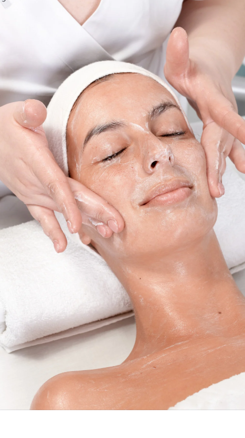 Woman receiving a facial treatment with a facial cleanser or moisturizer applied to her face, lying down with eyes closed, in a spa setting.