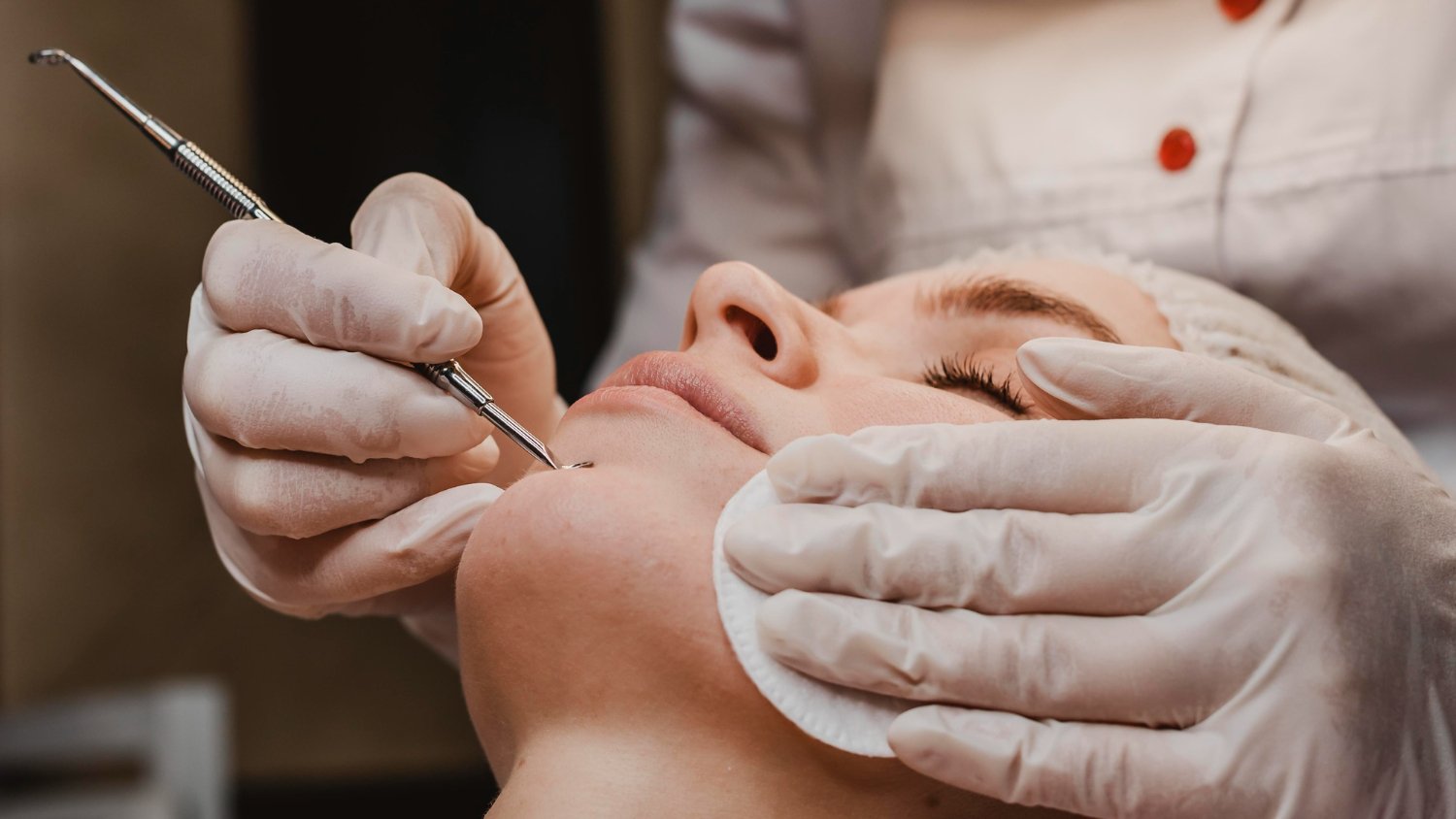 A person receiving a facial treatment, with a specialist using a tool on their face, while wearing gloves.