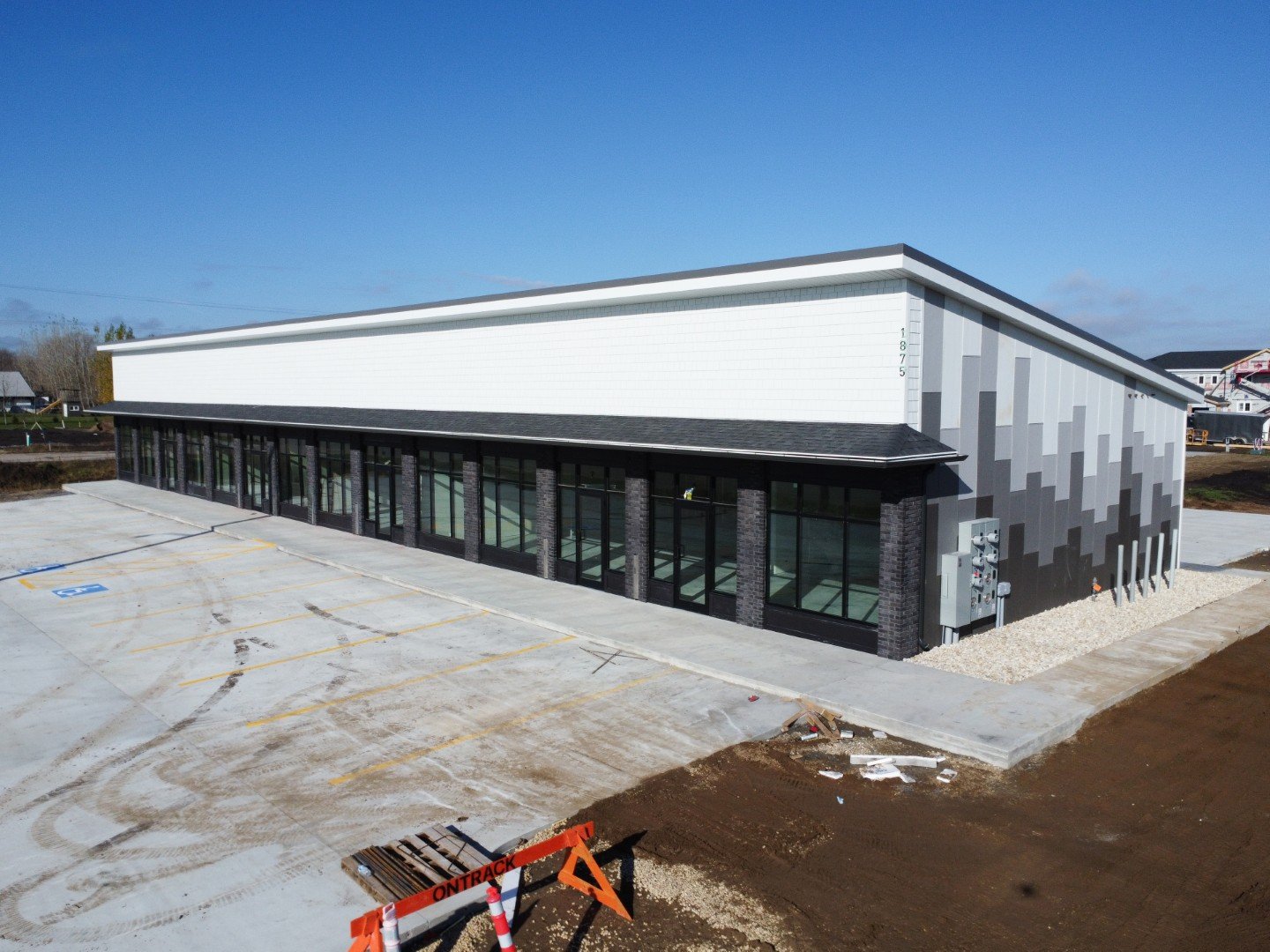 New commercial building with glass storefronts, black brick columns, and modern siding, under construction with vacant parking lot and construction signs.