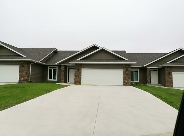 Property development home: front view of a modern suburban house with a concrete driveway, brick and siding exterior, and a garage door.