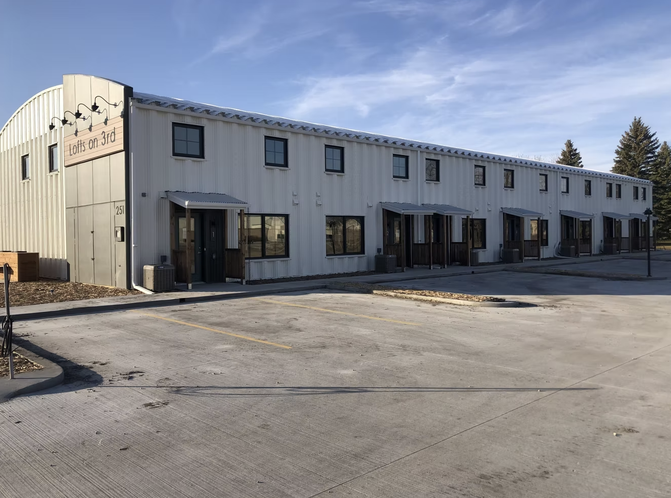 A two-story building with a metal exterior, multiple small windows, and concrete parking spaces in front, labeled "Lofts on 3rd".