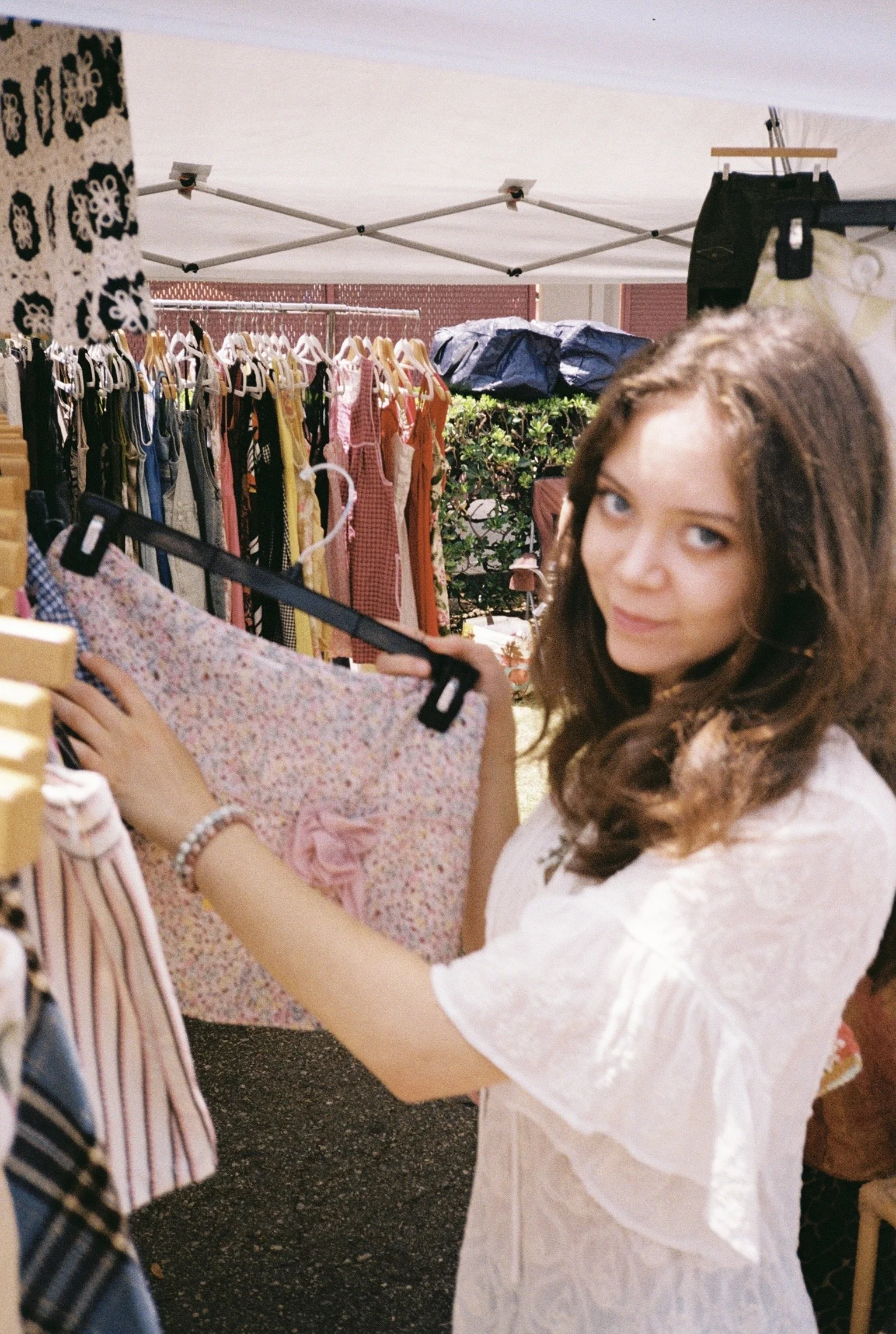 Young woman with brown hair shopping at an outdoor clothing market, holding a floral skirt.