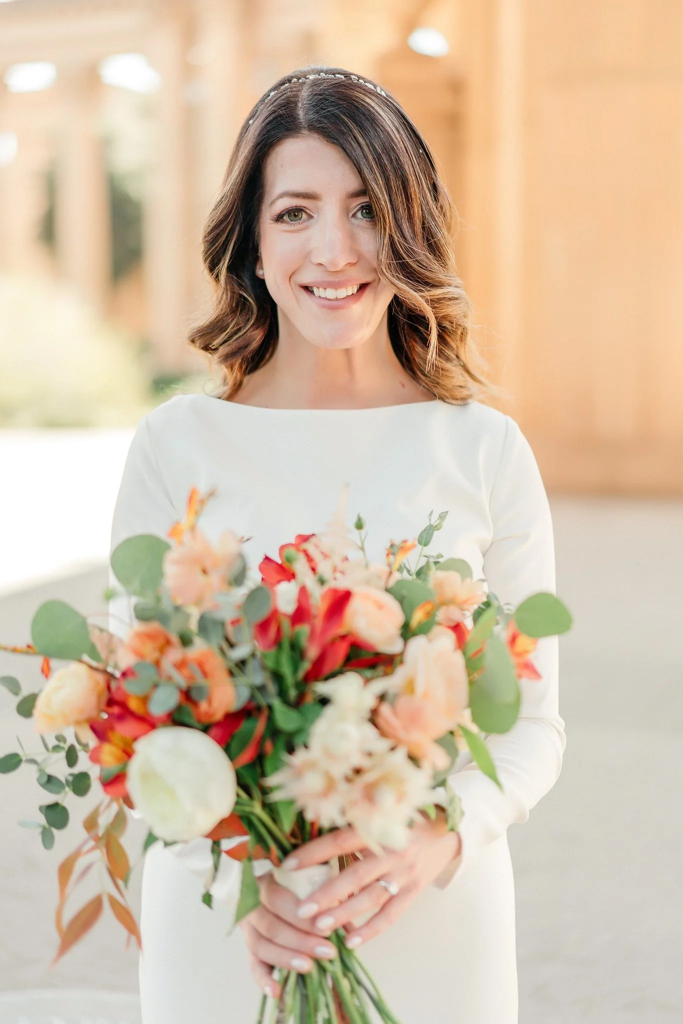 A smiling woman in a white dress holding a large bouquet of flowers.