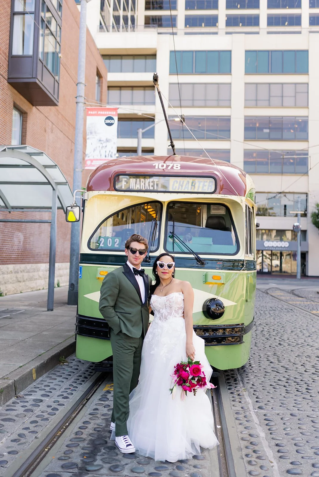 A couple in wedding attire posing in front of a vintage tram on a city street.