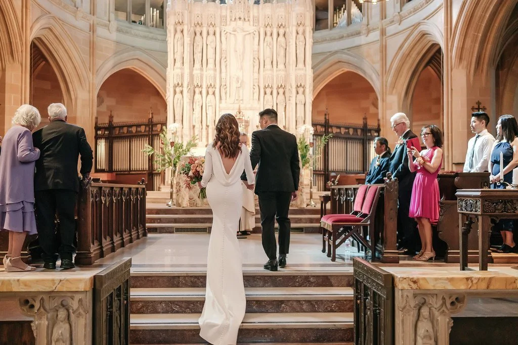 A bride and groom holding hands walking down the aisle in a church during a wedding ceremony, with guests seated on either side of the aisle.