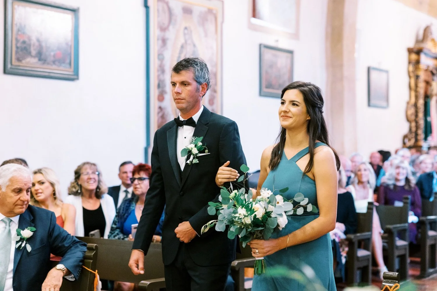 A bride and groom walking down the aisle during a wedding ceremony in a church, with guests seated and smiling in the background.