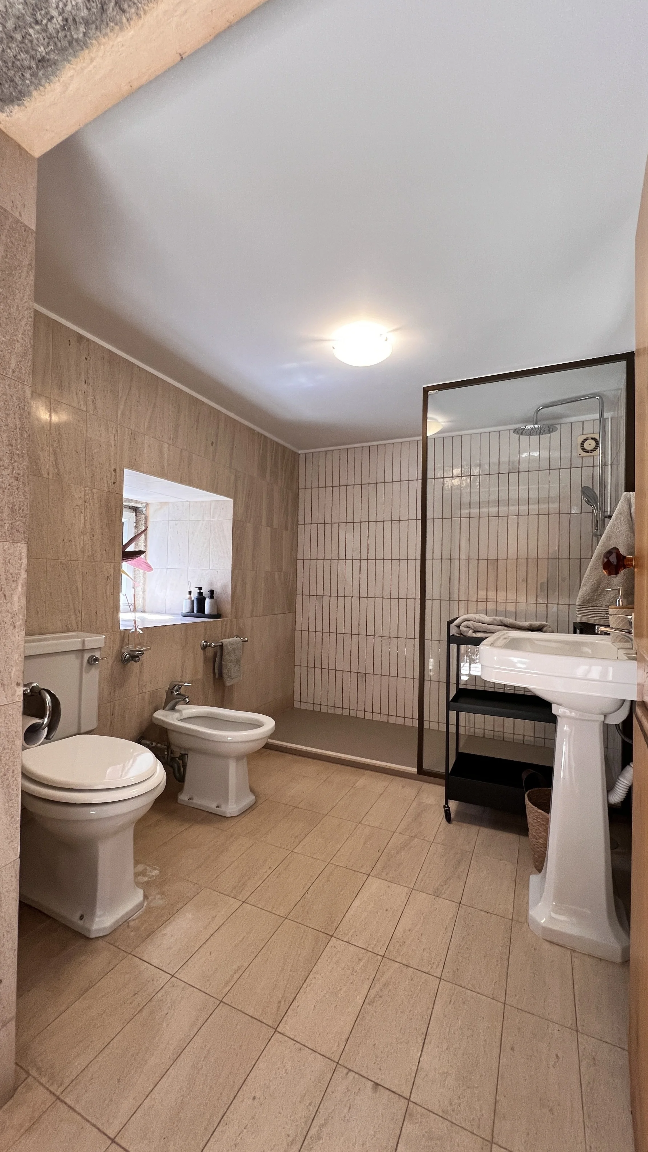 Quaint bathroom featuring sandstone tiles has a shower and bidet .