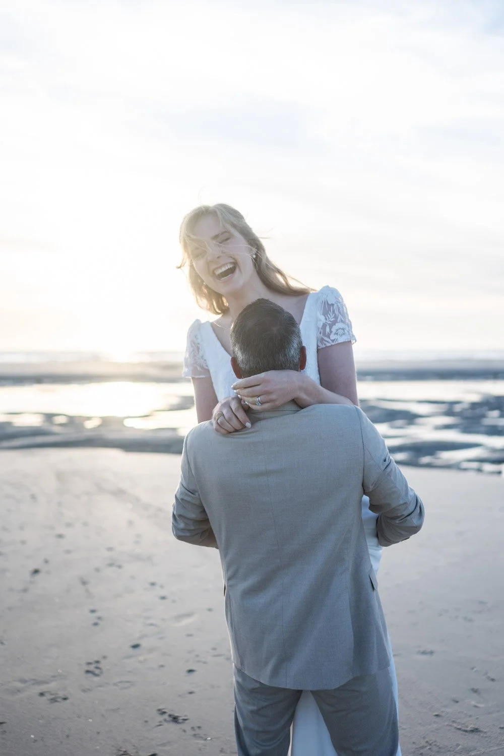 Couple de mariés rigolant. le marié tient la mariée dans ces bras et la fait tourner. Ils sont sur la plage en fin de journée