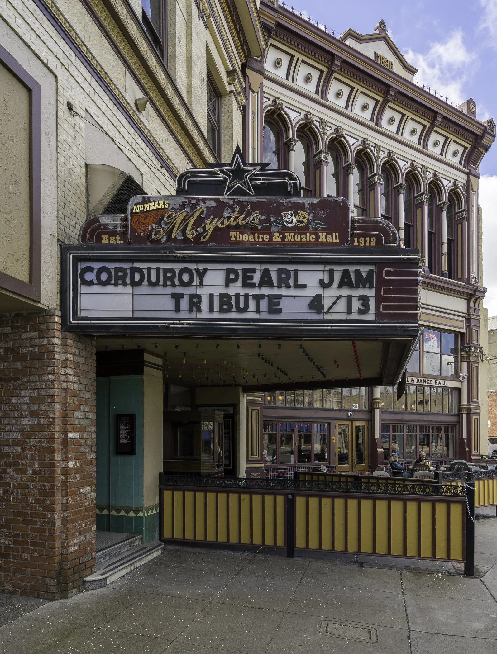 Marquee sign outside a theater advertising a Corduroy Pearl Jam tribute concert on April 13. The theater is called Mystic Theatre & Music Hall, established in 1912, with ornate architecture and outdoor seating area.
