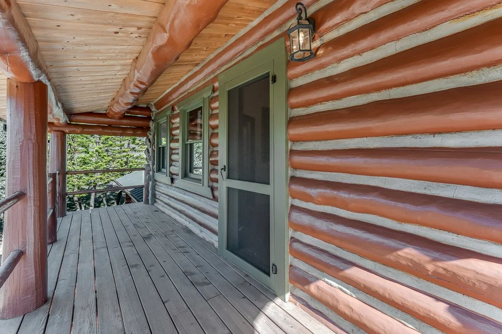 Wooden porch with log cabin siding, green-framed window, door, and outdoor lantern