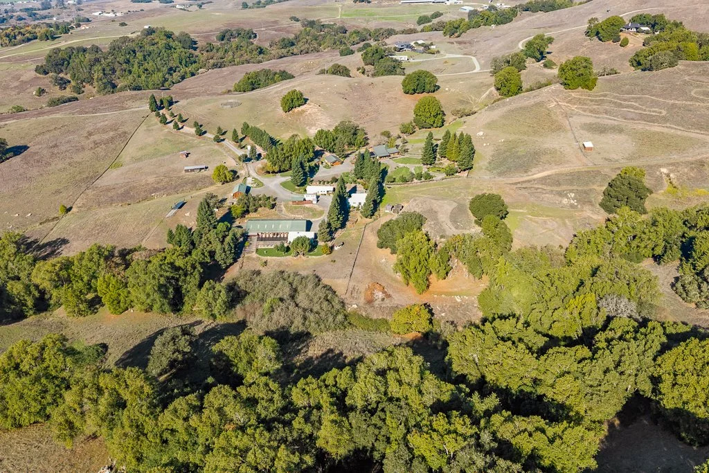 Aerial view of a rural landscape with rolling hills, scattered trees, and farm buildings.