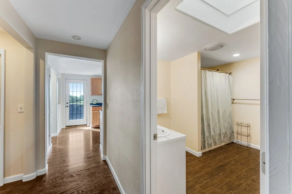 View of a hallway leading to a laundry room with a curtain-covered window and wooden flooring.
