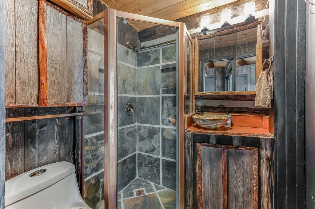 Small rustic bathroom with a corner shower, wooden paneling, a toilet, and a wooden vanity with a glass bowl sink.