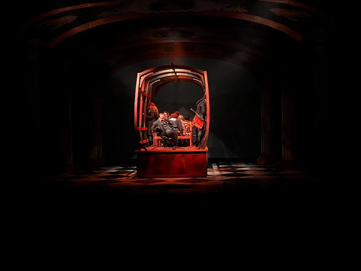 Theatrical performance with actors on stage inside a wooden structure, set in a dimly lit environment with a checkered floor.
