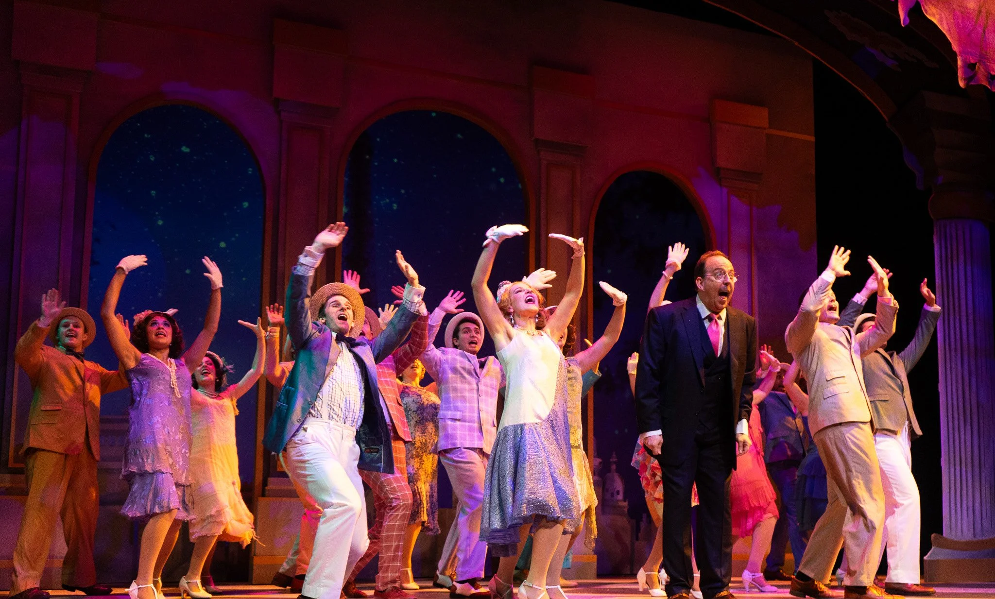 Actors performing on stage in colorful costumes with a starry night backdrop and architecture resembling a palace.