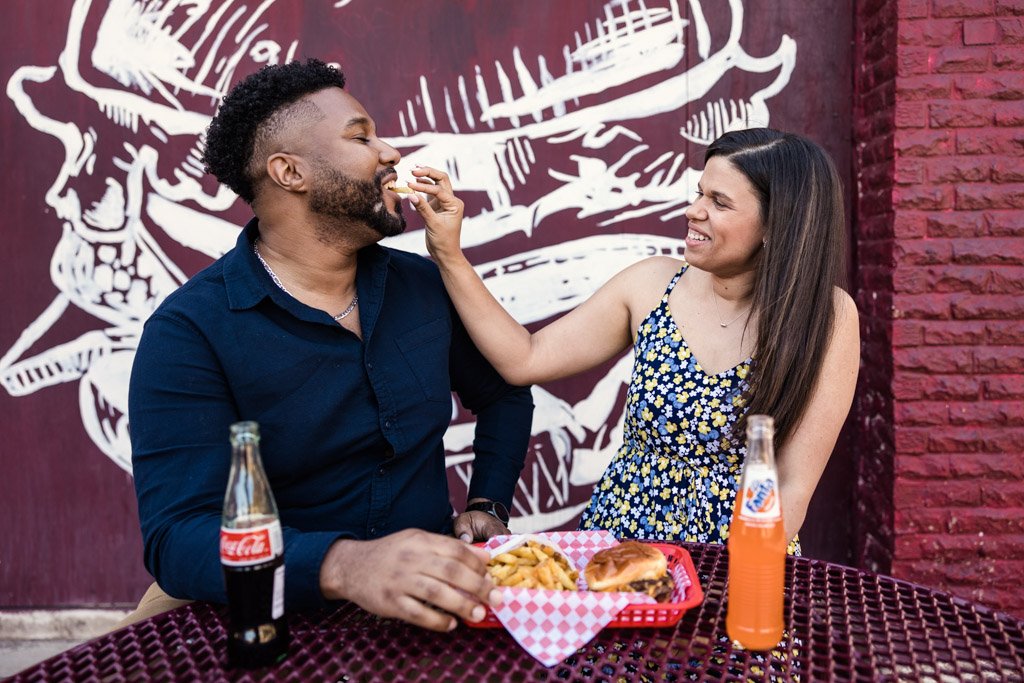 A man and woman laughing and having fun at a restaurant, with food and drinks on the table.