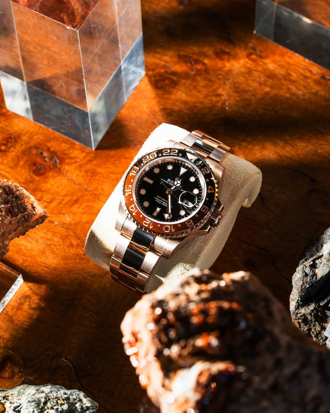 A luxury Rolex GMT-Master II wristwatch with a black dial, black and orange bezel, and two-tone metal bracelet displayed on a beige cushion.