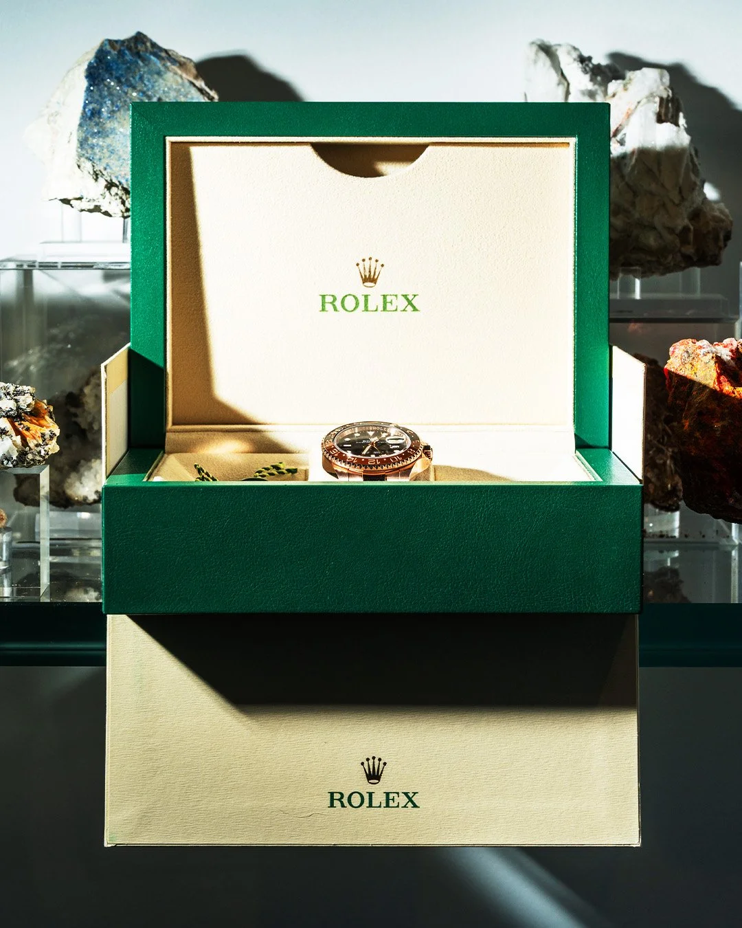 A Rolex watch in its green and cream box on display, with rock specimens in the background.