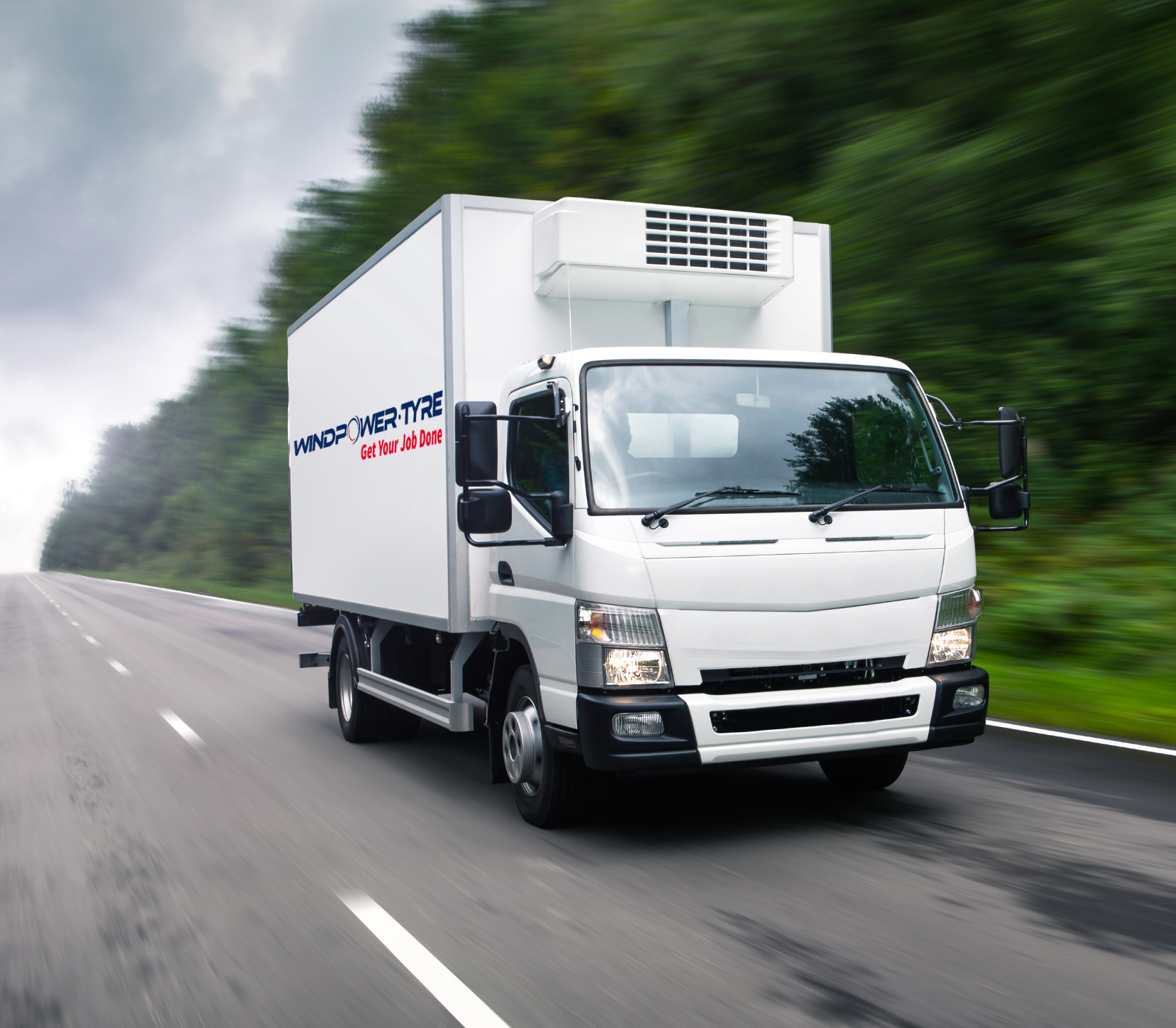 A white delivery truck with the logo 'WINDPOWER TYRE' and the slogan 'Get Your Job Done' on its side, driving on a highway with blurred green trees in the background.