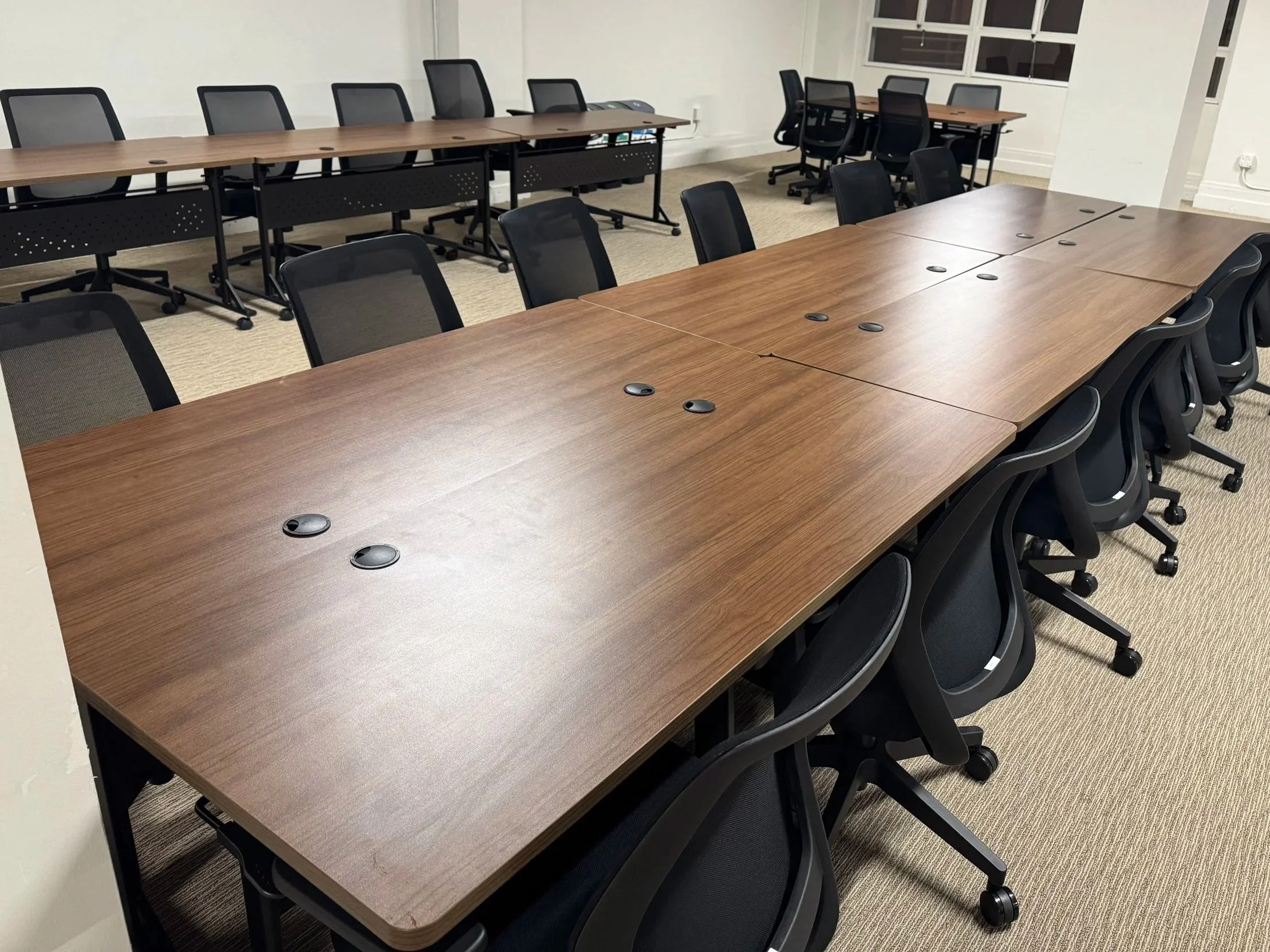 Empty conference room with wooden tables and black office chairs on a beige carpet.