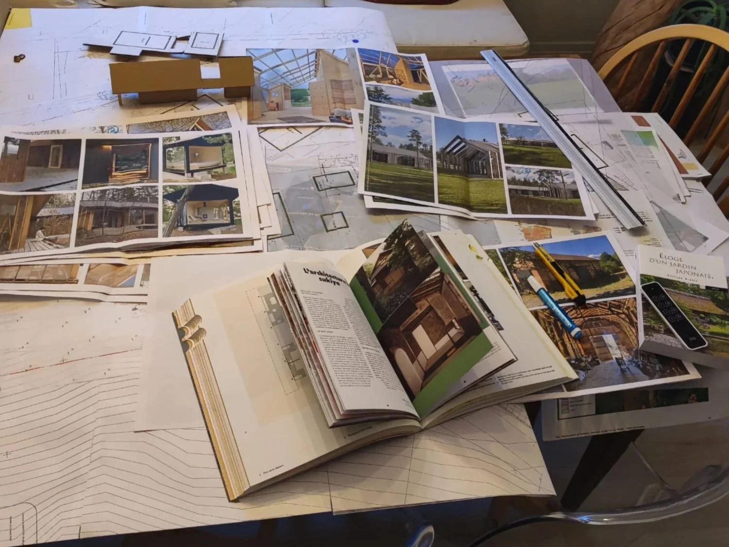 Table de travail avec plans architecturaux, images de bâtiments, règle, stylo, et livres d'architecture.