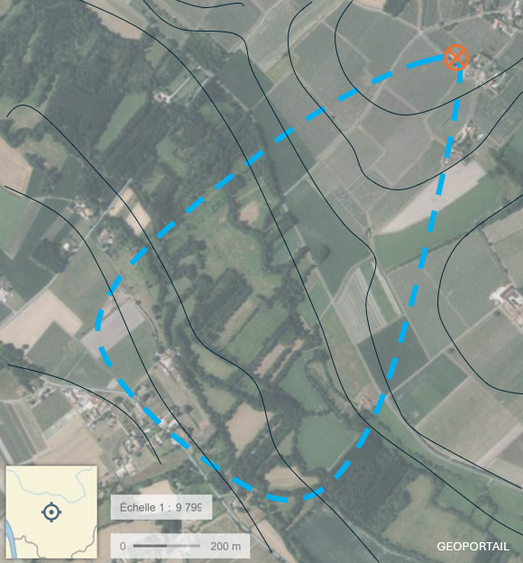 Carte aérienne avec contours topographiques, un tracé en pointillé bleu indiquant un chemin ou une zone délimitée, et un symbole de croix orange en haut à droite.