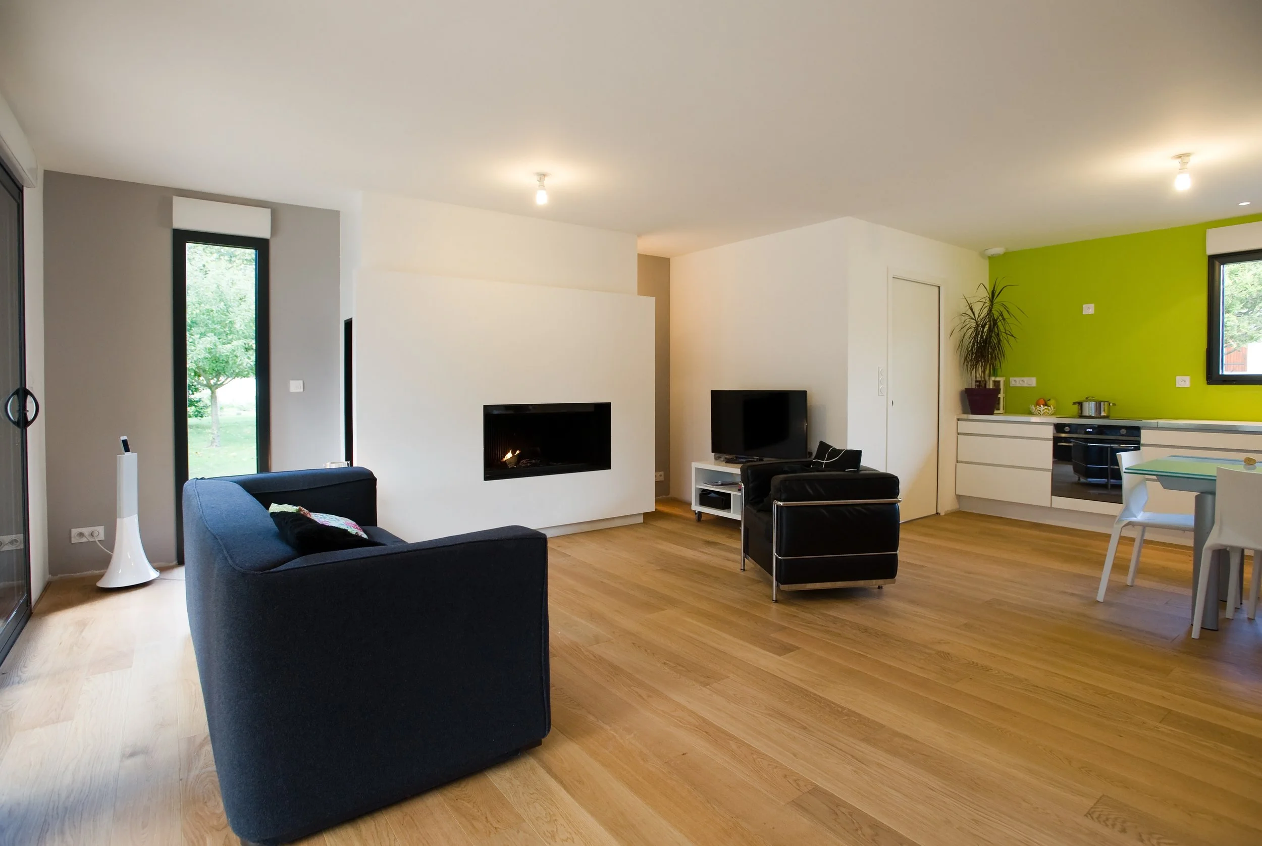 Salon contemporain avec canapé noir, cheminée encastrée, télévision, murs blanc et vert