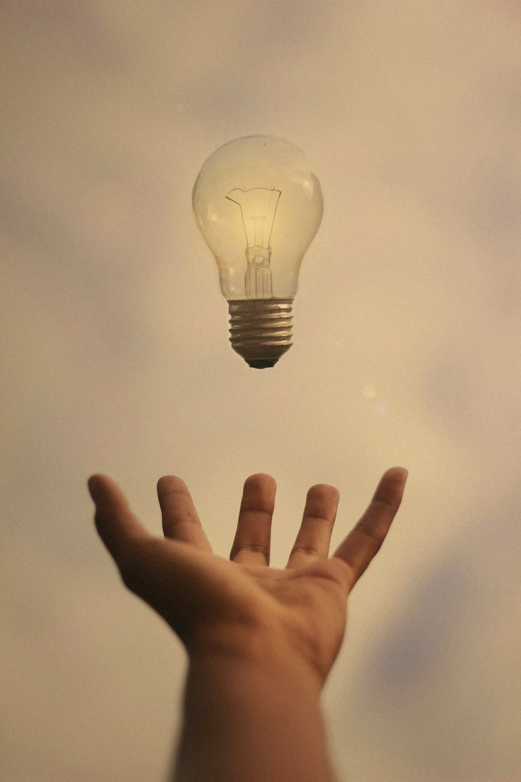 A hand is catching a floating light bulb against a plain background.
