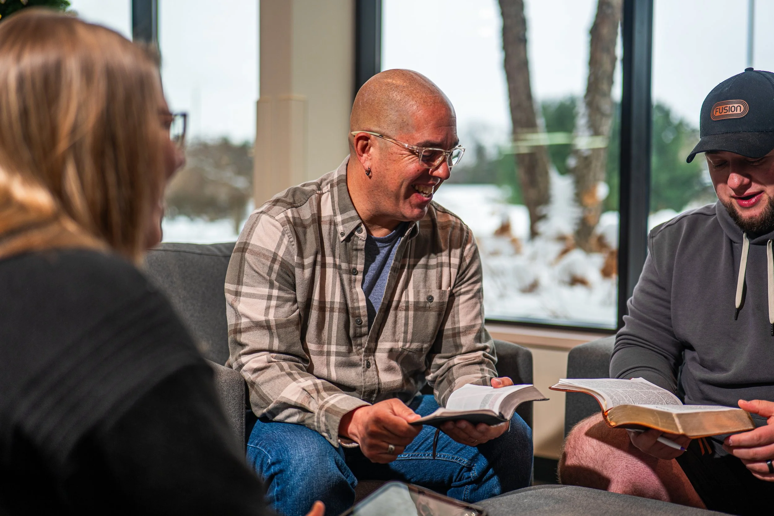 Three people sitting on a couch inside, holding books and smiling during a group discussion.