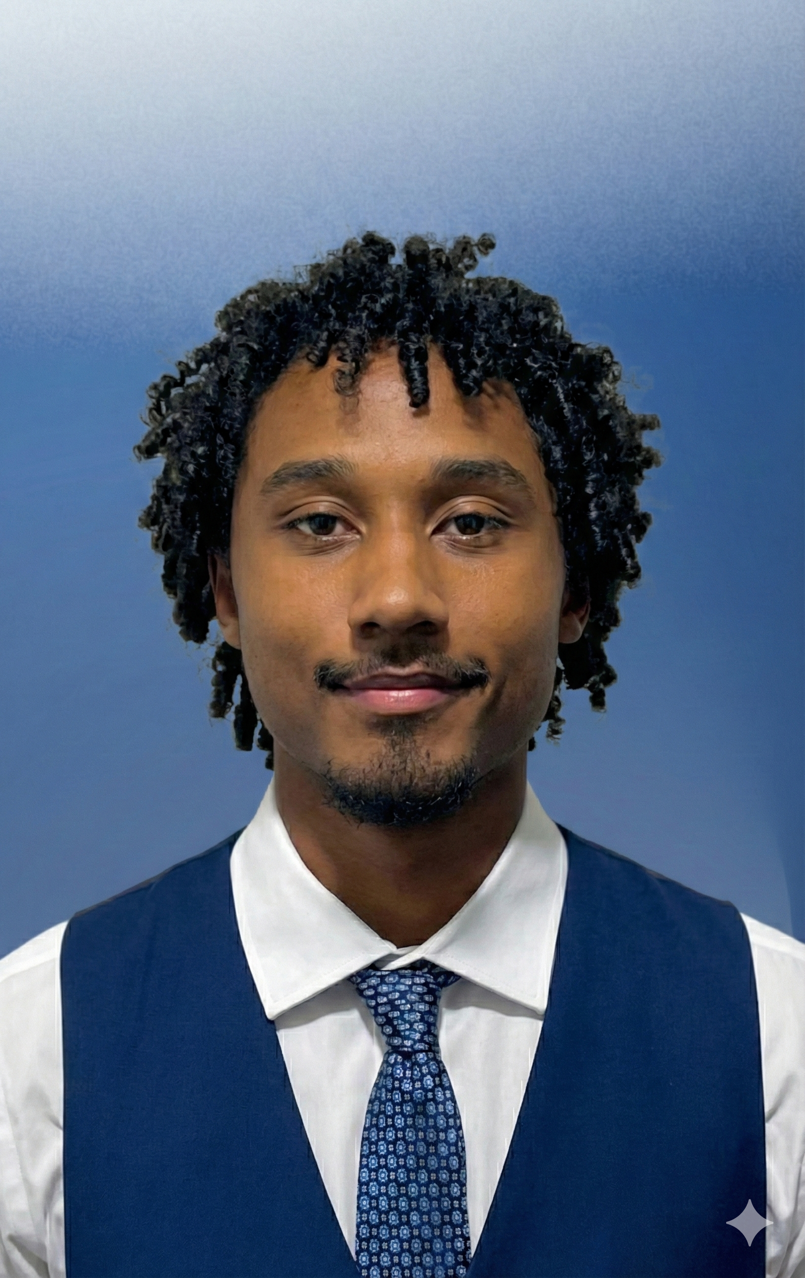 Portrait of a young man with curly hair, wearing a white shirt, blue vest, and a patterned blue tie, against a blue gradient background.