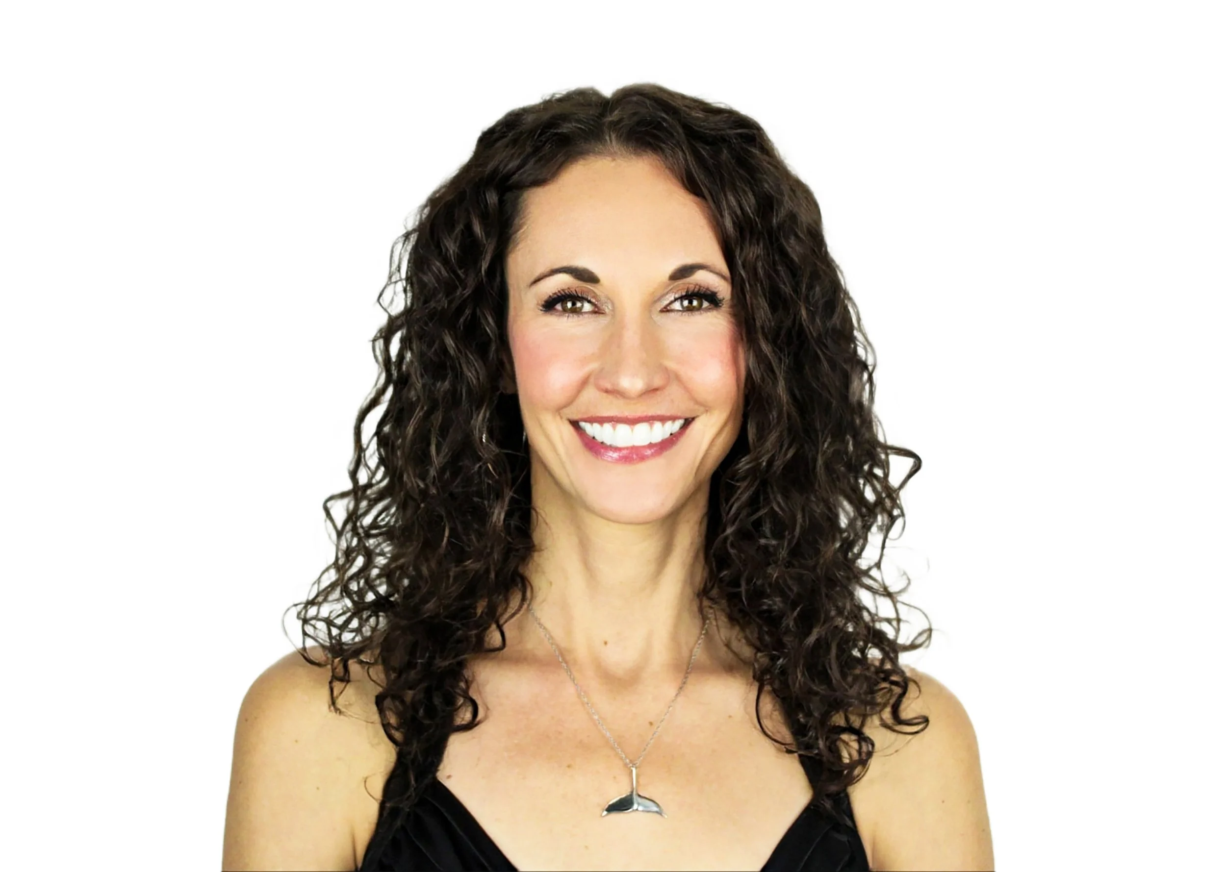 Studio headshot of a woman named Michelle Rau with long, dark shoulder-length curly hair, warm brown eyes, and a broad smile, wearing a dark top and a silver whale tail necklace against a clean white backdrop.