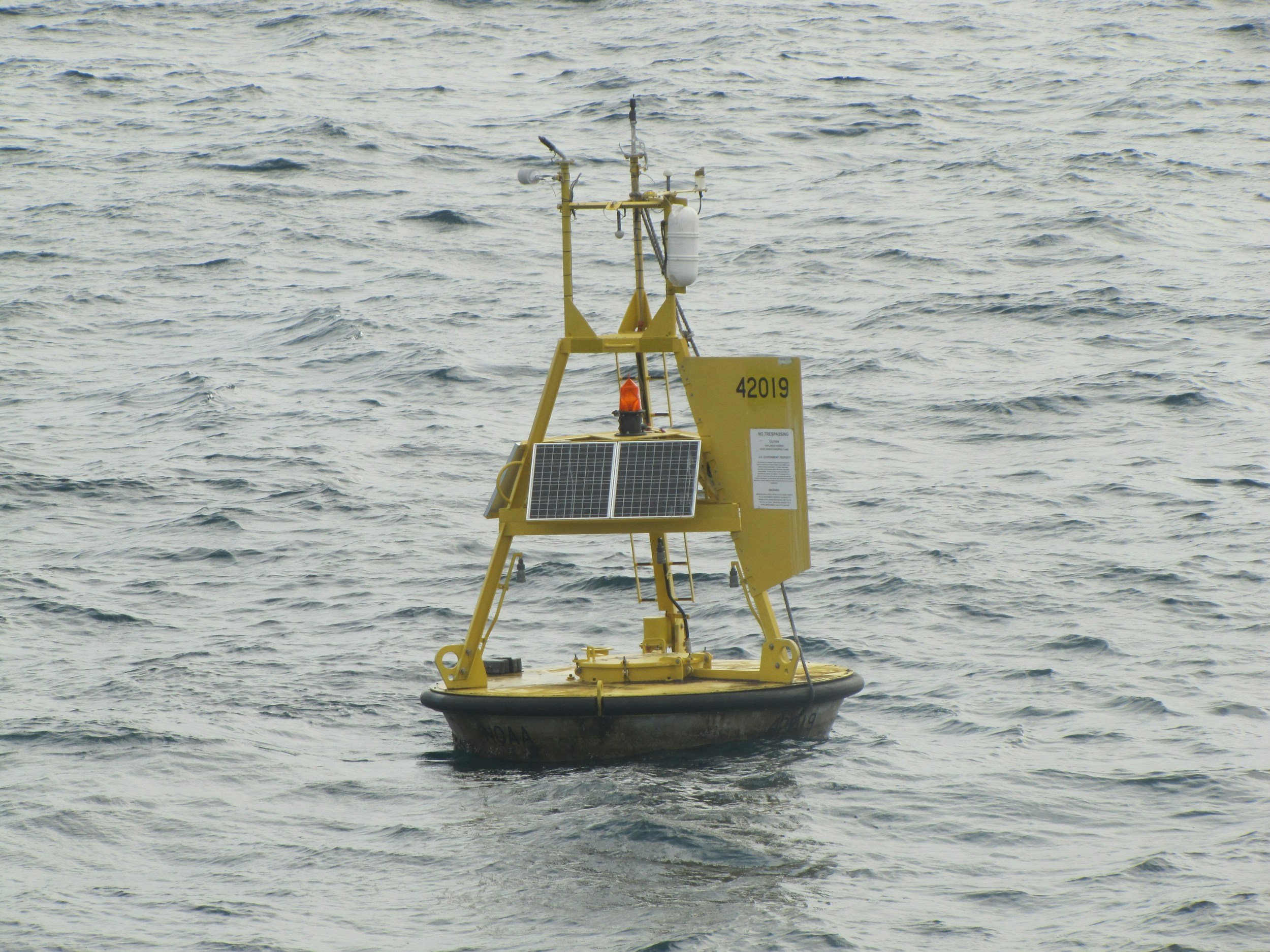 A yellow unmanned marine drone floating in the ocean, equipped with sensors, solar panels, and communication equipment.