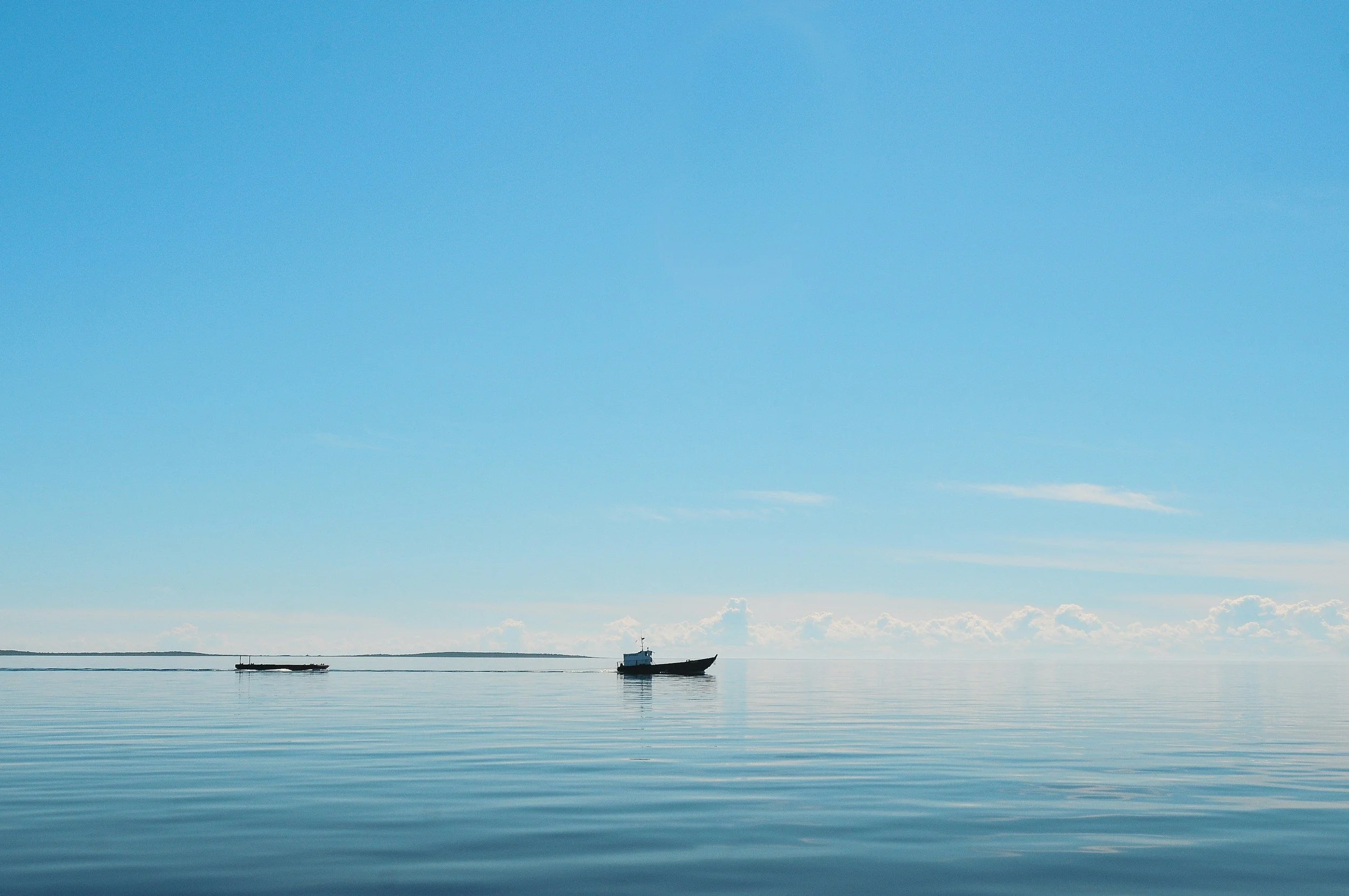 Calm ocean water with two boats, one larger and one smaller, under a mostly clear sky with few clouds.