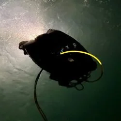 A black diving mask with a yellow snorkel attached, submerged underwater.