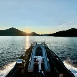 View from the front of a boat on a body of water during sunset, with mountains in the distance.
