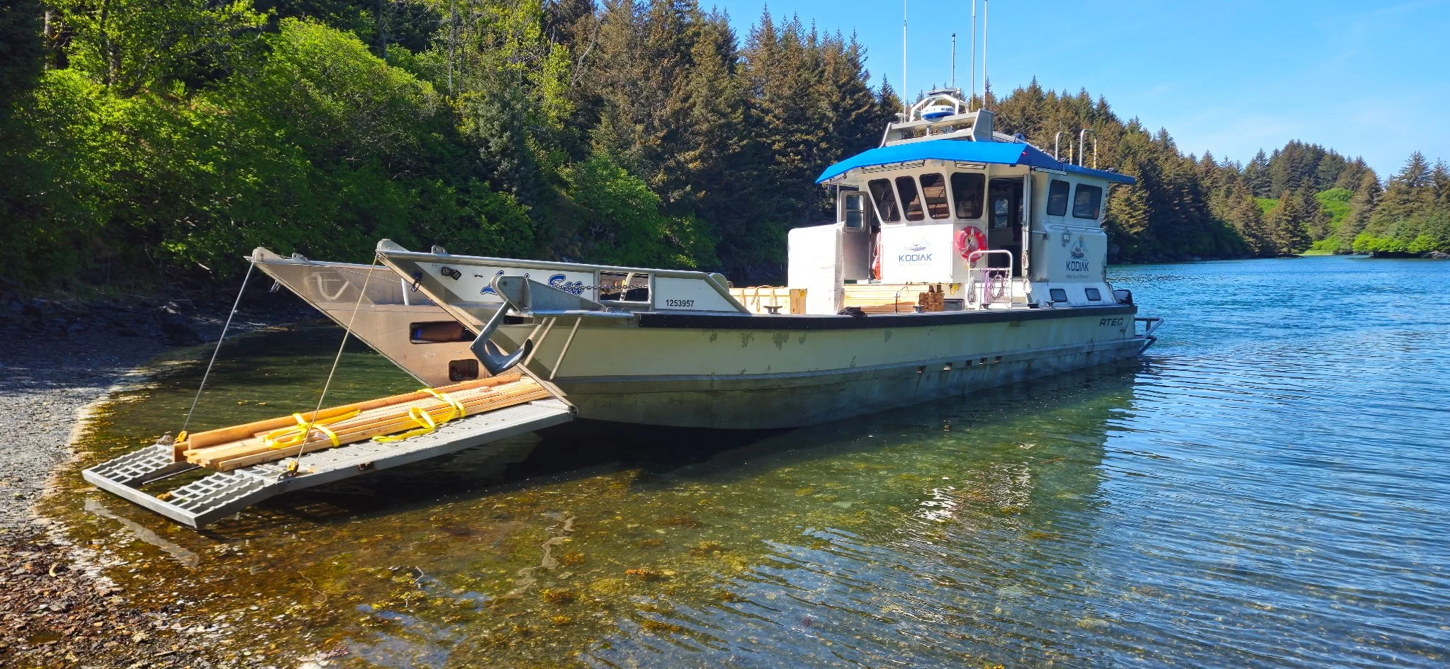 A boat docked at the shore of a lake with trees in the background and clear blue sky.