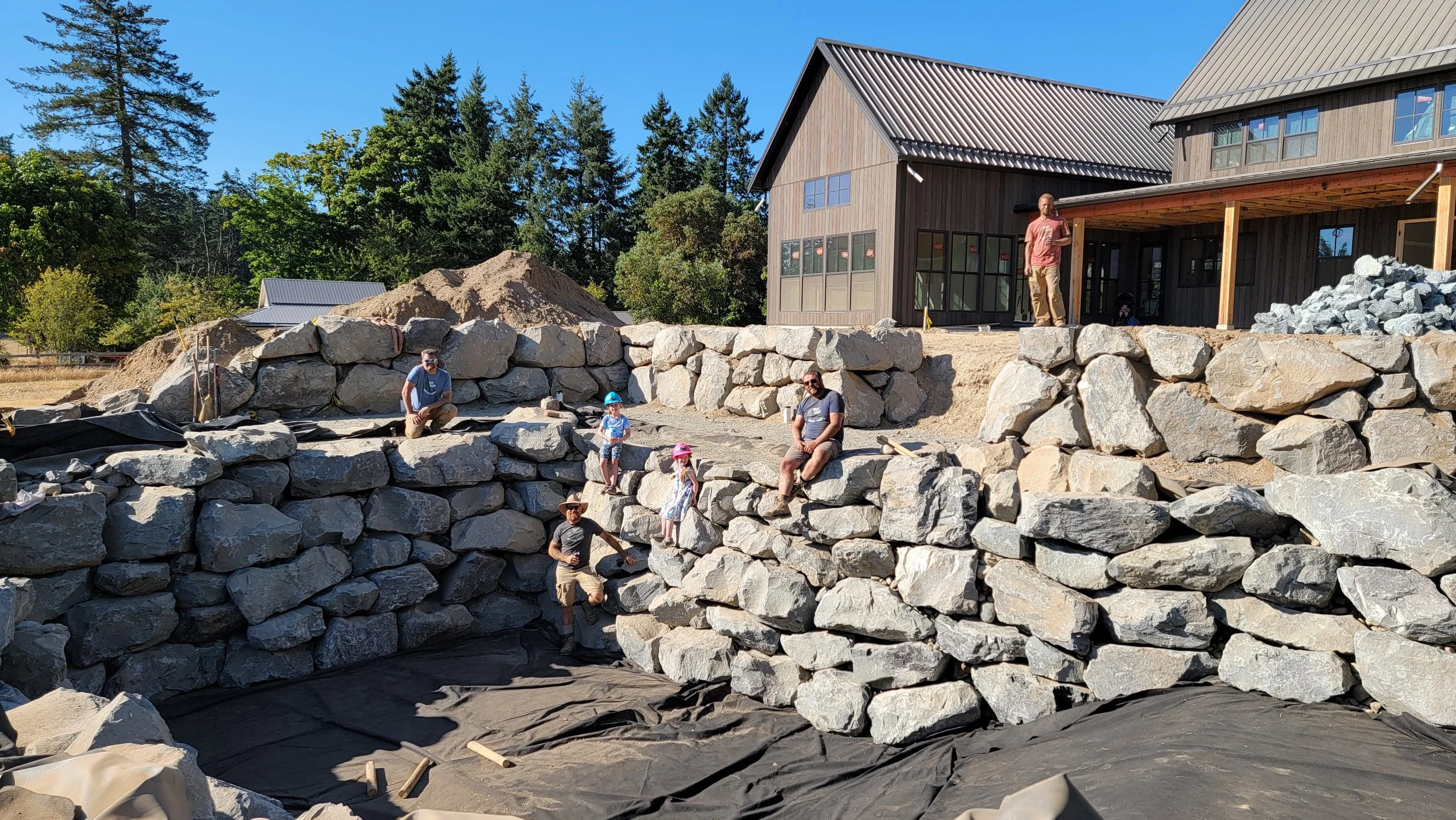 Natural swimming pool under construction with liner installation and rock and boulder retaining wall in progress