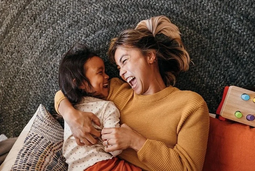 Mother and daughter laughing and hugging on the floor, representing parent support and children therapy