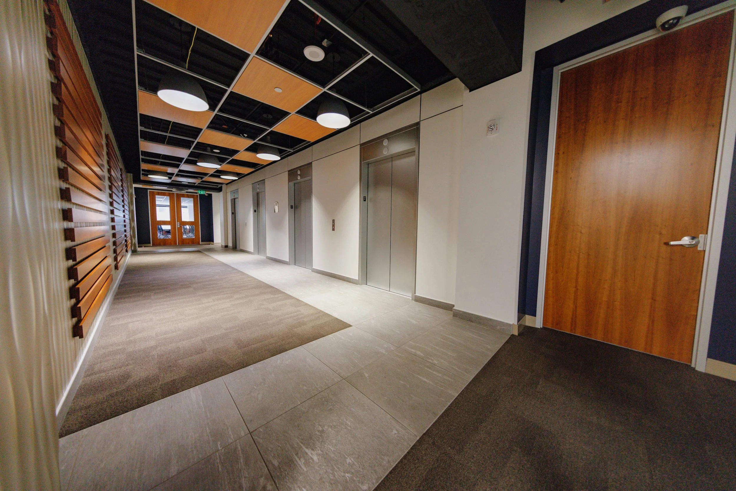 Hallway with elevator doors, wooden door, and modern ceiling design with lighting fixtures.