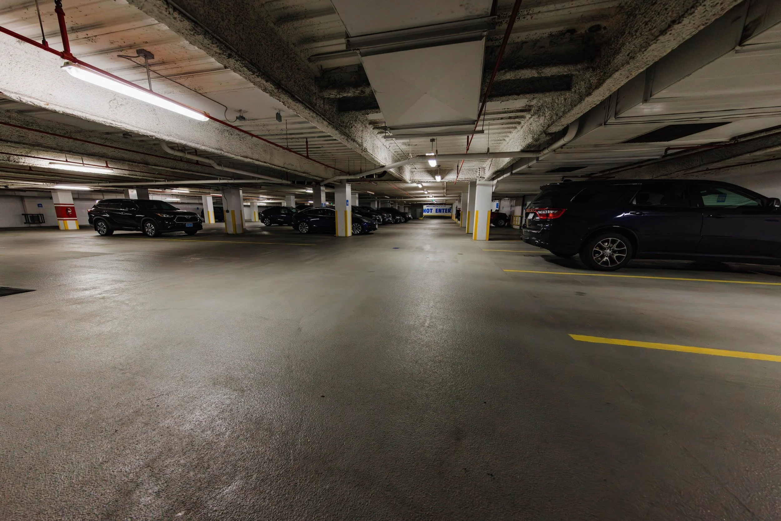Underground parking garage with parked cars on both sides, yellow parking lines, support columns, and a 'Do Not Enter' sign at the end of the aisle.