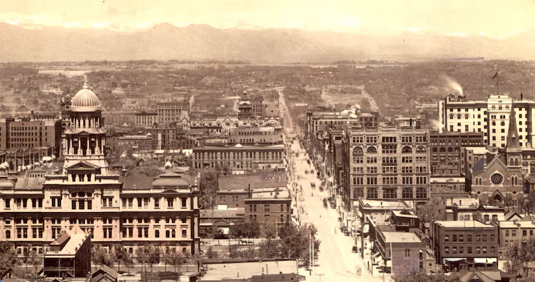 Historical black and white photo of a cityscape with a prominent domed building on the left and a straight main avenue leading to distant hills.