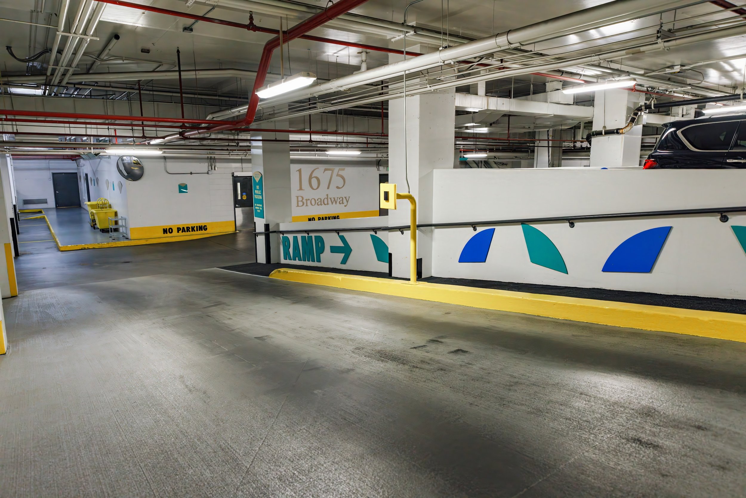 Underground parking garage with a ramp, directional sign pointing right, and parked cars in the background.