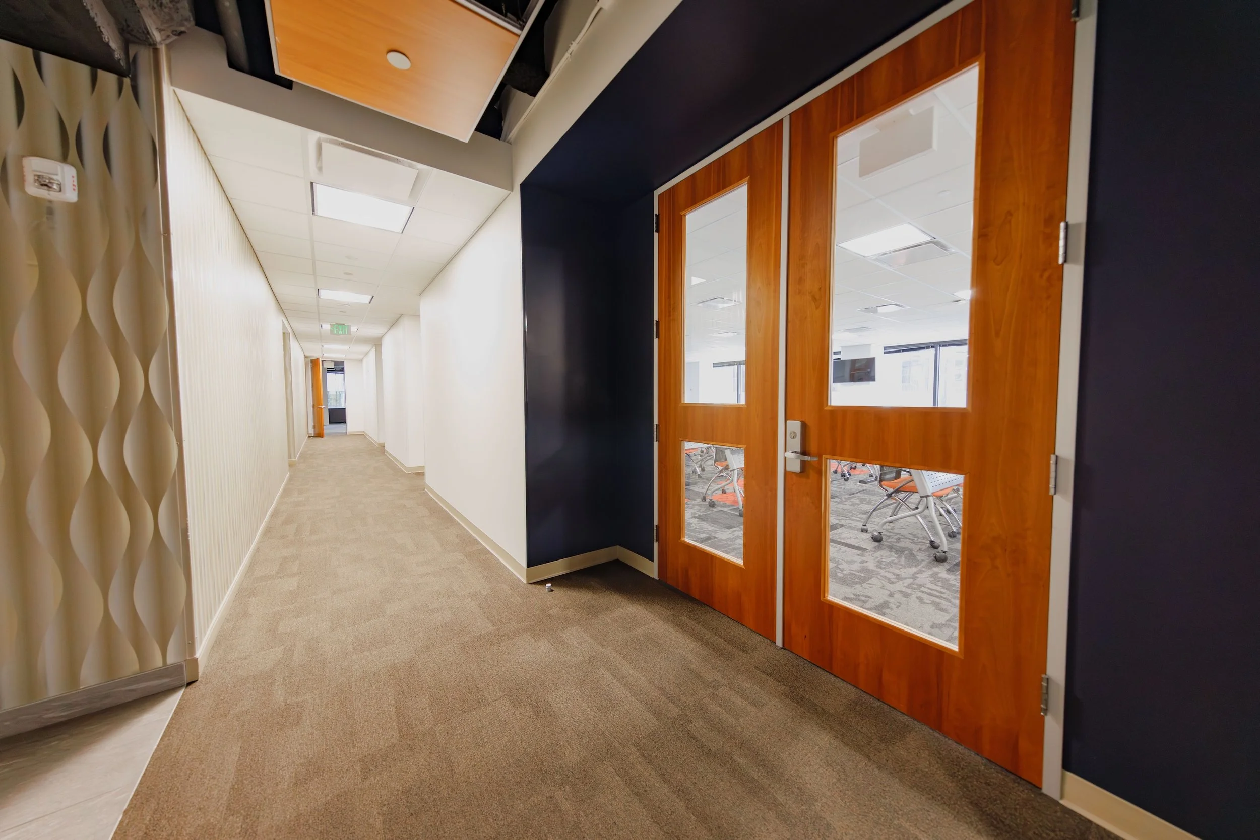 A hallway in an office building with wood-framed glass double doors leading into a conference room or office space.