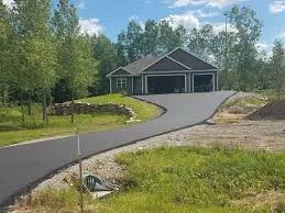 Newly paved driveway leading to a garage with a house and trees in the background