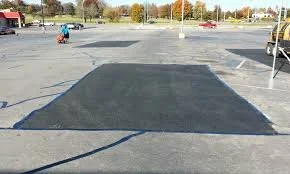 Empty parking lot with a freshly paved section and a shopping cart and a pole in the background.