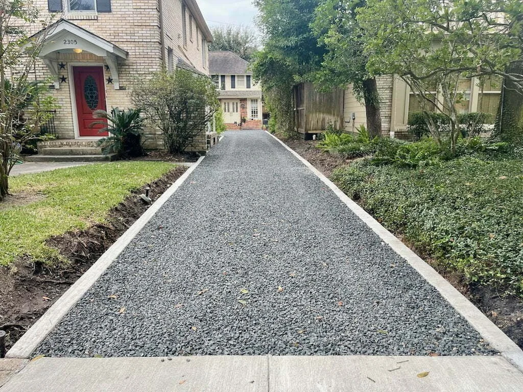 A gravel driveway leading to a house with a red front door, surrounded by greenery and trees.