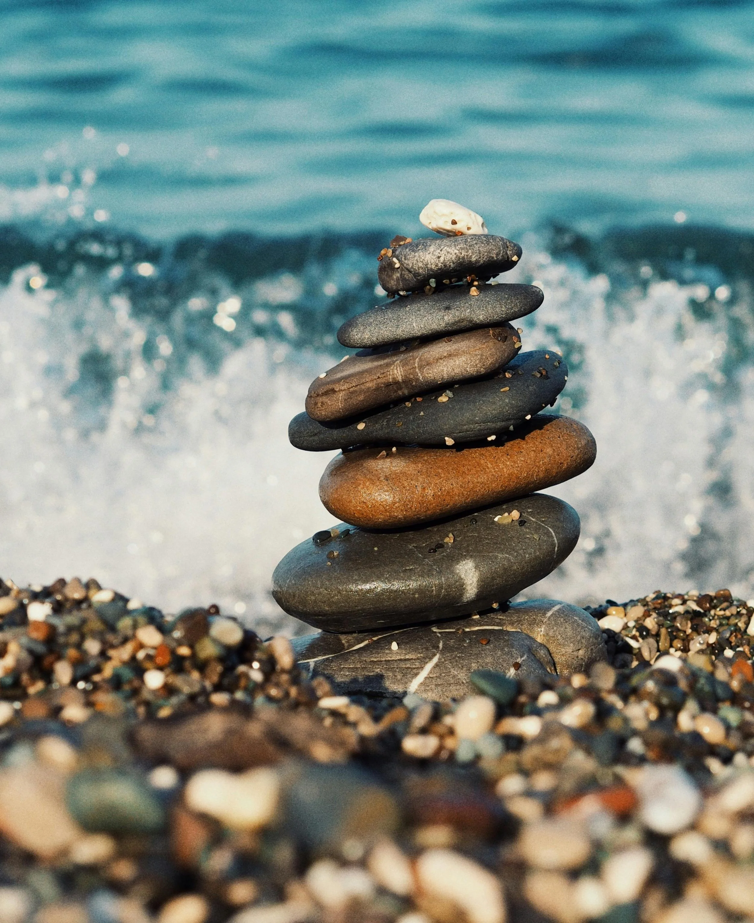 Stacked stones on a pebbled beach with ocean waves in the background.